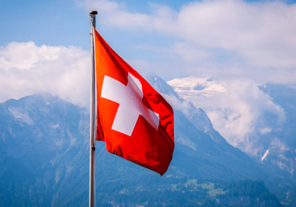 Swiss,Flag,Waving,With,Mountains,Background